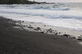 Waves rolling onto a black sand beach strewn with rocks and pebbles in Hana Bay, Maui Royalty Free Stock Photo