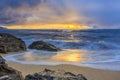 Waves rolling onto a rocky beach with a fiery sunset and rain in background in North Shore Oahu, Hawaii, long exposure Royalty Free Stock Photo