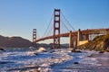 Waves rolling into shore of sandy beach with view of Golden Gate Bridge at sunset Royalty Free Stock Photo
