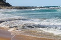 Waves rush onto shore over flat volcanic rocks with more rocks jutting out into the sea