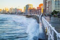 Waves splashing against the wall in San Lorenzo beach in Gijon, Asturias, Spain, with the promenade and buildings in one side