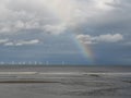 Waves washing on the shore with a beautiful rainbow above and wind turbines on the horizon Royalty Free Stock Photo