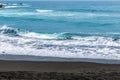 Waves with white foam on the crests of the sea with blue water and black sand Royalty Free Stock Photo