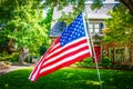 Waving American Flag large  in front of blurred upscale two story landscaped home with car behind security gate surrounded by Royalty Free Stock Photo