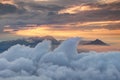 Waving clouds, jagged peaks and orange sky above morning mist Royalty Free Stock Photo