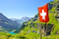 Waving flag of Switzerland on the hill in Swiss Alps. Turquoise Oeschinensee in background. National concept. Switzerland summer.