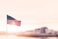 Waving flag of United States of America in focus. Modern town out of focus in the background. Warm sunny day. Sun flare. Abstract Royalty Free Stock Photo