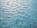 Waving pattern of vivid turquoise blue water in the swimming pool above stone tiles with soft light of reflection of the sunshine