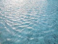 Waving pattern of vivid turquoise blue water in the swimming pool above stone tiles with soft light of reflection of the sunshine