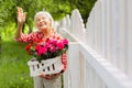 Beaming elderly lady waving to her neighbor standing near fence