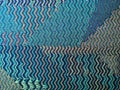 Wavy distortion effect of a green, beige and blue woven cloth rug.
