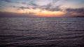 The wavy water surface of the Black Sea against dramatic clouds and sky of the setting sun. Lights of the city Adler in the Royalty Free Stock Photo