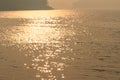 Wavy water surface with glittering orange sun light and black mountains in the background.