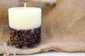 Wax beautiful light beige candle with unflavored wick from below decorated with coffee beans on the background of old brown canvas Royalty Free Stock Photo
