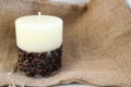 Wax beautiful light beige candle with unflavored wick from below decorated with coffee beans on the background of old brown canvas Royalty Free Stock Photo