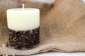 Wax beautiful light beige candle with unflavored wick from below decorated with coffee beans on the background of old brown canvas Royalty Free Stock Photo