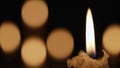 Wax burning candle flickers in dark on a black background with blurred candlelight bokeh effect. Background or