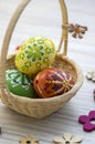Wax painted Easter eggs in light brown wicker basket, wooden flower decorations Royalty Free Stock Photo