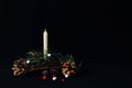 Wax white candle, pine branch decorated with colorful balls, fir cones on dark background. Symbolic concept first Advent,