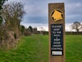 A way marker indicates a public footpath ahead, fixed to a wooden post in a field in winter