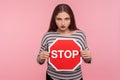 Way prohibited! Portrait of angry strict bossy woman in striped sweatshirt holding red Stop symbol and . indoor studio shot