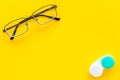 Way to improve vision. Contact lenses in container near glasses on yellow background top view copy space