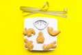 Ways for lose weight. Sport. Cookies in shape of yoga asans near scale and measuring tape on bright yellow background