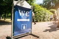 WC sign board stands on sandy pathway and human queue