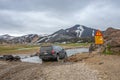 4WD car is crossing a river near major campsite in colorful rainbow volcanic Landmannalaugar mountains with thousands tourists and