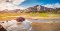 4WD car is crossing a river near major campsite in colorful rainbow volcanic Landmannalaugar mountains with thousands tourists and