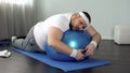 Weak-willed fat man relaxing on fitness ball, home workout break, laziness Royalty Free Stock Photo