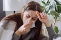 Weakened immune system concept. Close up of sick female seated sitting on couch in living room covered with plaid sneezing holding Royalty Free Stock Photo