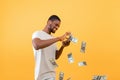 Wealth concept. Young rich black guy throwing out money bills, standing over yellow studio background