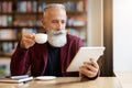 Wealthy grey-haired elderly man drinking coffee and using digital tablet Royalty Free Stock Photo