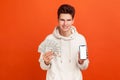 Wealthy self confident teenager in casual hoodie holding fan of dollars and smartphone with blank display, betting, easy earnings