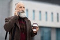 Wealthy senior man with coffee to go having business call