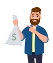 Wealthy and successful young man is holding money, cash bag in hand and pointing hand index finger towards. Business, banking. Royalty Free Stock Photo