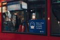 Wear a face mask sign on the window of a red double decker bus in London, UK