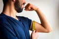 Bearded thin man measuring biceps, muscles of his left arm with a yellow tape measure. He`s smiling, happy. Royalty Free Stock Photo