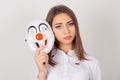 Wearing a mask, faking it concept. Closeup portrait worried girl with sad expression holding a clown mask expressing happiness,