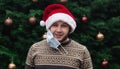 Wearing a mask incorrectly. Close up Portrait of man wearing a santa claus hat, xmas sweater and medical mask with emotion.