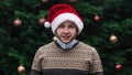 Wearing a mask incorrectly. Close up Portrait of man wearing a santa claus hat, xmas sweater and medical mask with emotion.