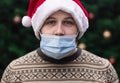 Wearing a mask incorrectly. Close up Portrait of man wearing a santa claus hat, xmas sweater and medical mask with emotion.