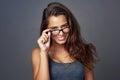 Wearing twice as many eyes. Studio portrait of an attractive young woman peering over her glasses against a grey Royalty Free Stock Photo