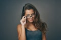 Wearing twice as much eyes. Studio shot of an attractive young woman peering over her glasses against a grey background. Royalty Free Stock Photo