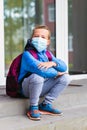 Wears face mask sad schoolkid boy child resting outdoors. Bored little student on the stairs look at camera Royalty Free Stock Photo