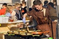 Weary cook prepares meat dishes in cast iron pans in outdoor kitchen