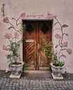 Weather worn wooden door with artwork roses and real flowers in ornate urns in medieval town in Europe