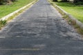 a weathered asphalt path with signs of wear and patchwork, and overgrown grass Royalty Free Stock Photo