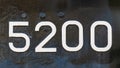 Weathered numbers zero, two, five, 5200, or 5, 2, 0 painted white on a piece of black metal. Abstarct numeral background